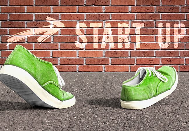 1 Paar grüne Turnschuhe laufen auf eine beschriftete Backsteinmauer zu. "Start Up"
