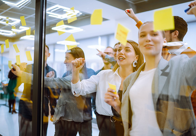 Eine Gruppe junger Menschen stehen vor eine Glasscheibe und bekleben diese mit PostIts
