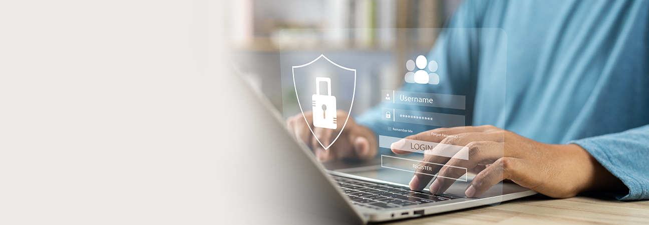 Eine Person tippt auf einem Laptop, während ein transparentes, digitales Anmeldefenster mit einem Schutzschild-Symbol und Login-Feldern eingeblendet ist.